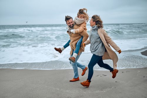A mom, dad, and daughter run on the beach during the winter in Old Saybrook, CT.