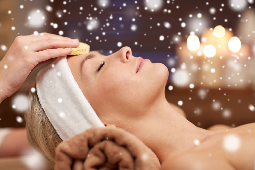 A woman's smiling face is seen during a Saybrook spa visit, with snow flurries in the forefront and background.